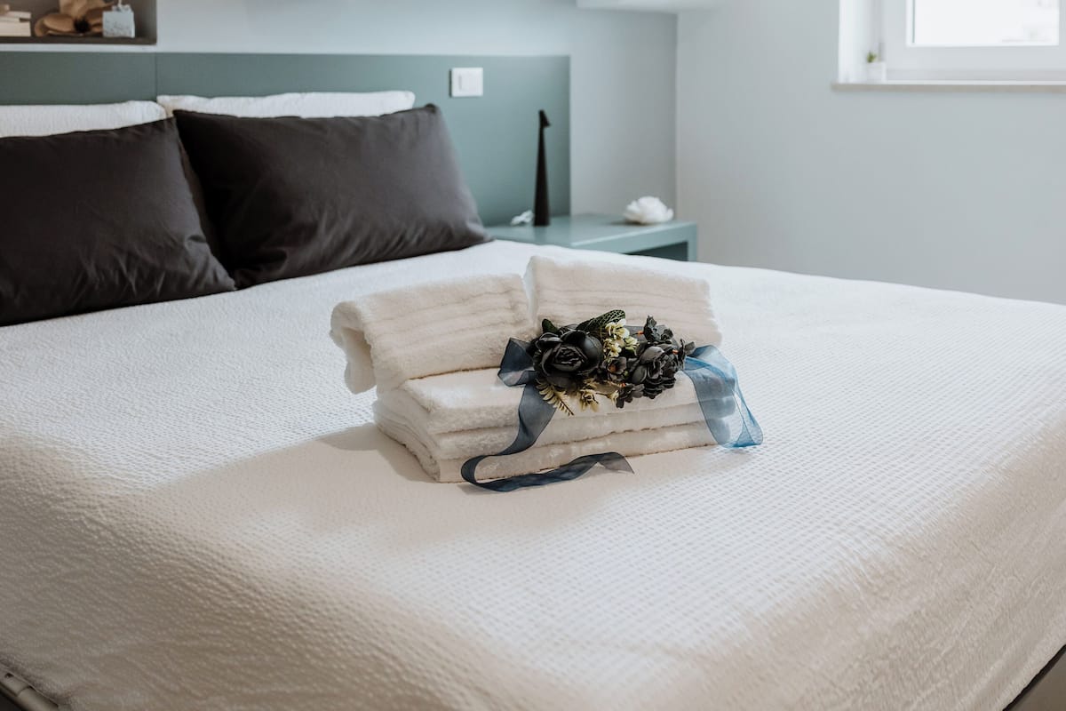 A neatly made bed with a white comforter and a bouquet of flowers.