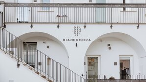 Un bâtiment dont la façade porte l’inscription « BIANCOMORA », et qui se distingue par un escalier avec des rampes en métal et des portes en arc de cercle.