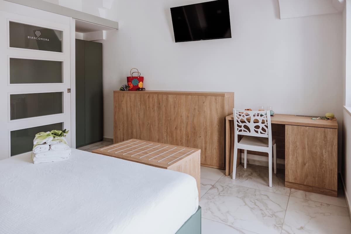 A bedroom with a bed, a wooden desk, a chair, a TV, and a wardrobe.