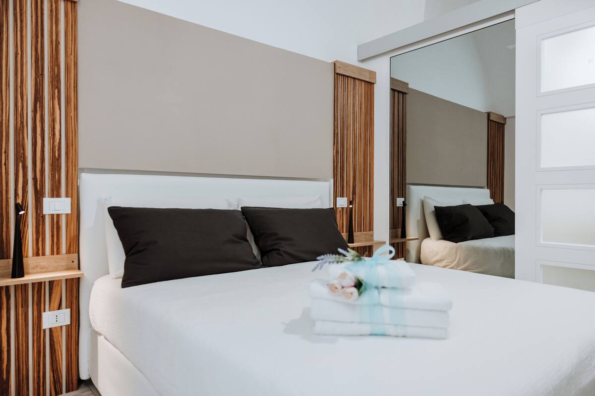A modern hotel room with a large bed, wooden paneling, and a mirror.