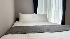 A neatly made bed with white bedding and a gray throw blanket, positioned in a room with a window and sheer curtains. - Yui-Takasaki (Takasaki)