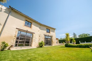 Edifici de dues plantes amb grans finestres, teulada plana i un jardí ben cuidat amb plantes en testos.