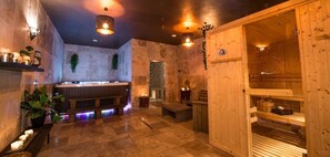 Una sala de sauna amb bancs de fusta, un banc amb cadira de massatge, una porta de fusta i una prateleira amb espelmes.