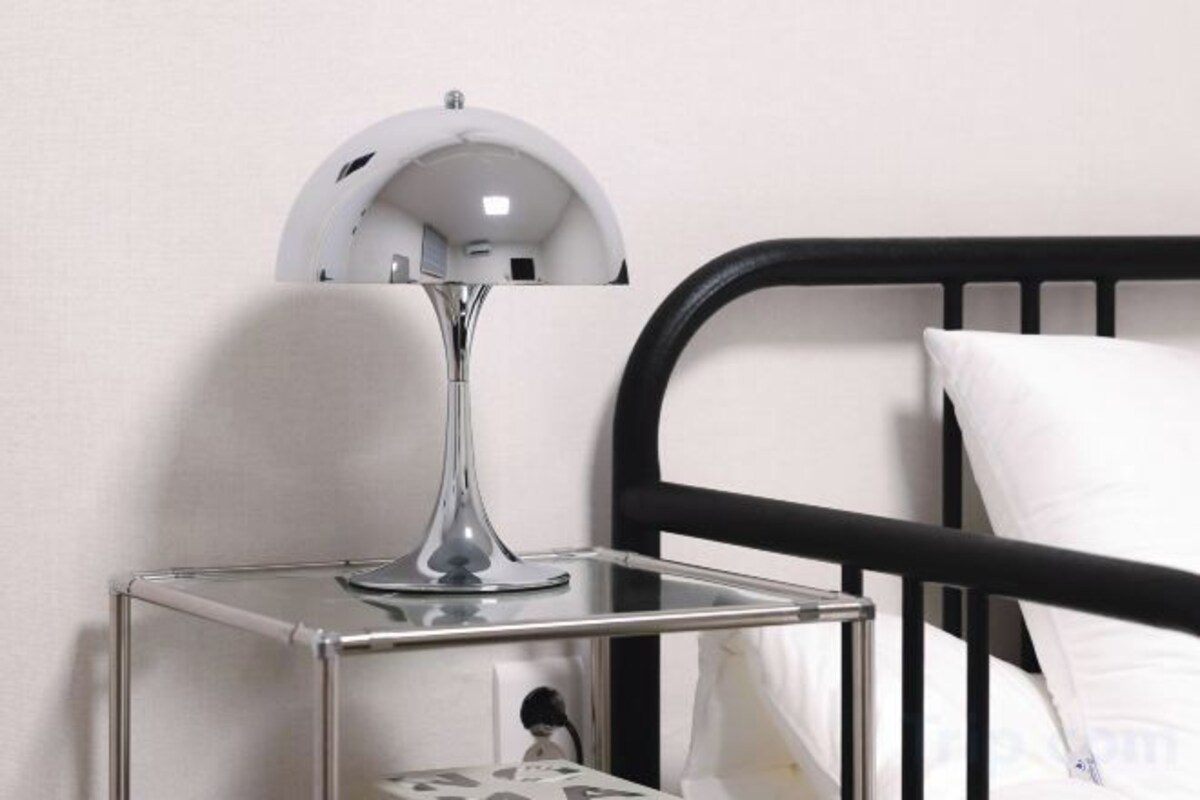 A bedside table with a lamp, a bed with a black frame, and a white pillow.