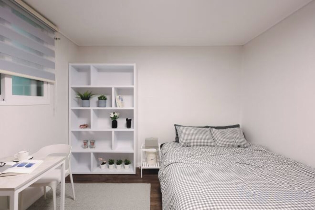 A bedroom with a bed, a desk, and a shelving unit.