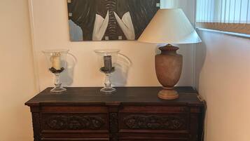 A wooden dresser with two glass vases and a lamp, a painting on the wall, and a radiator.