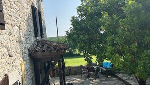 Ein Steingebäude mit einer Terrasse, die einen Tisch, Stühle, eine Pergola und einen Blick auf ein grünes Feld bietet.