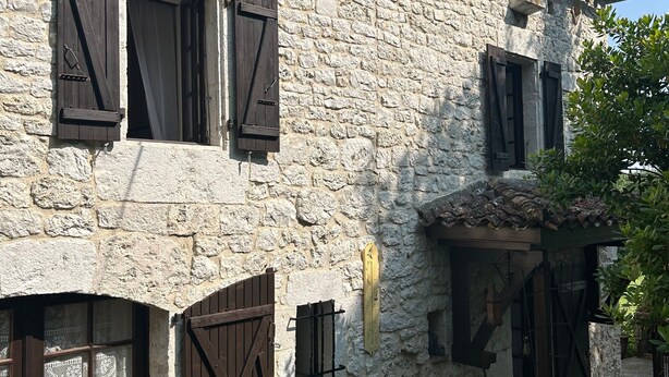 Ein Gebäude aus Stein mit hölzernen Fensterläden, einem kleinen Tisch und Blumentöpfen davor.