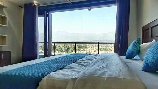 Une chambre d’hôtel avec un grand lit, une vue sur les montagnes par la fenêtre et un balcon avec une balustrade.