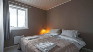 Ein Schlafzimmer mit Bett, einem Fenster mit Vorhängen, einem Heizkörper und einer Nachttischlampe.