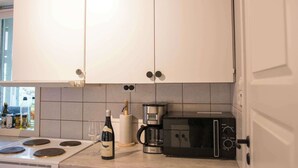 A kitchen with white cabinets, a stove, a microwave, a coffee maker, and a wine bottle. - Practical 3-Beds Apartment in Tromsø (Tromsø)