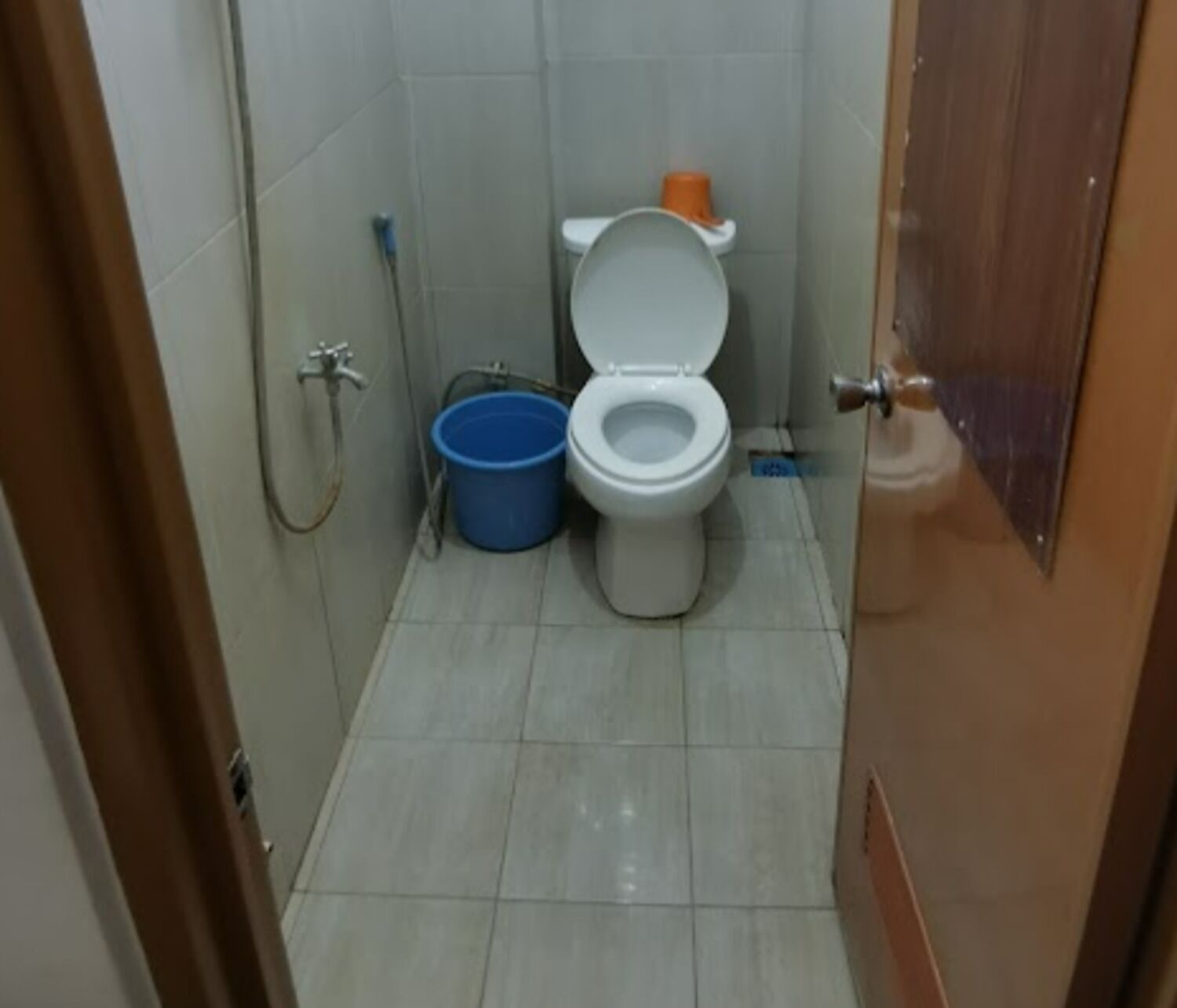 Un baño pequeño con un inodoro, un cubo azul y una manguera de ducha.