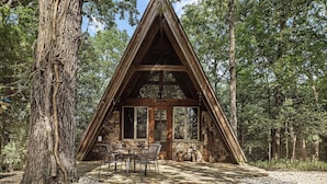 A wooden cabin with a triangular roof, large windows, and a stone exterior, surrounded by trees. - Secluded Cabin with Hot Tub, Firepit (Murray)