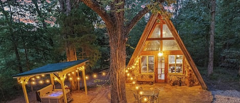 Une cabane chaleureuse avec des fondations en pierre, une terrasse en bois et des guirlandes lumineuses.