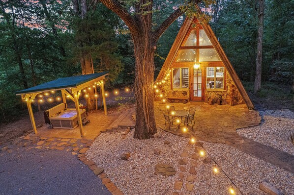 Une cabane chaleureuse avec des fondations en pierre, une terrasse en bois et des guirlandes lumineuses.
