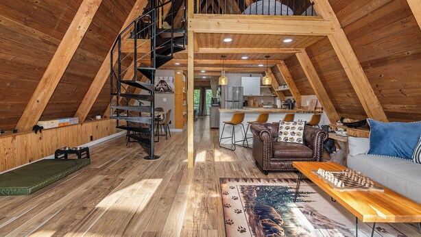 A spacious loft with a wooden interior, a spiral staircase, a dining area, and a kitchen. - Secluded Cabin with Hot Tub, Firepit (Murray)