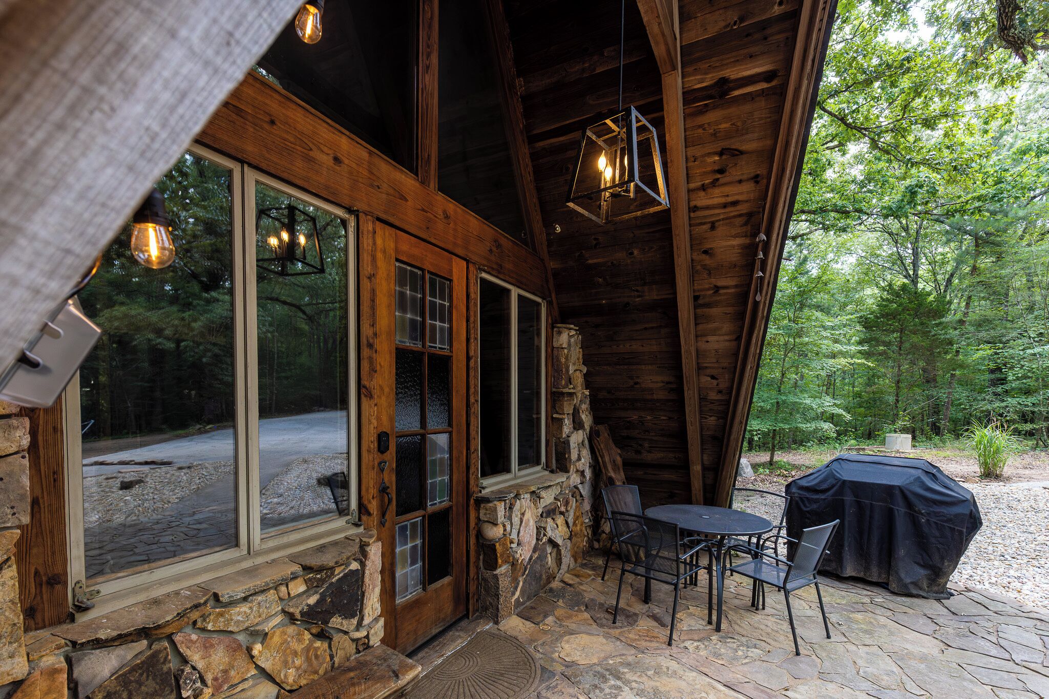 A rustic wooden cabin with large windows, stone walls, and a patio area with outdoor seating.