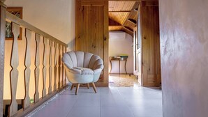 Un couloir au plancher de bois, avec un fauteuil blanc et une rambarde en bois.