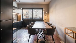 A modern kitchen with a long wooden table, black cabinets, and a large window with a view of buildings. - Licia (Rome)