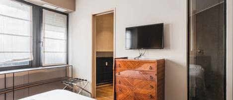 A modern hotel room with a bed, a wooden dresser, a TV, and a shower.