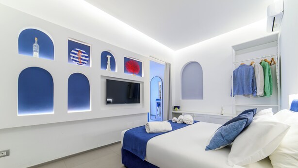 A modern hotel room with a neatly made bed, a television, and a wardrobe with hanging clothes.