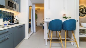 A modern kitchen with blue cabinets, a microwave, and a white countertop. There are two blue bar stools and a white table with a vase of flowers.