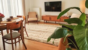 A living room with a wooden dining table, chairs, a sofa, a television, and a large plant. - FLH Harmony Suite by PGE National Stadium (Warszawa)