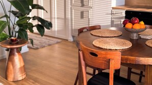 A wooden dining table with woven placemats, surrounded by chairs. A bowl of fruit is placed on the table. - FLH Harmony Suite by PGE National Stadium (Warszawa)