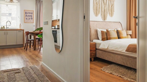A modern hotel room with a large bed, bedside table, and a view of the kitchen and dining area. - FLH Harmony Suite by PGE National Stadium (Warszawa)