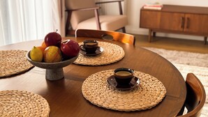 A dining table with a woven placemat, a bowl of fruit, and two cups of coffee. - FLH Harmony Suite by PGE National Stadium (Warszawa)