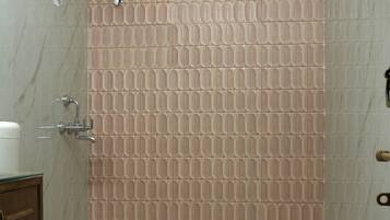 Un baño con inodoro, ducha y grifo empotrado en la pared, y piso de baldosas.