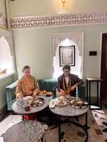 Two people dining at a table with a variety of dishes, in a room with a green sofa and a decorative ceiling.