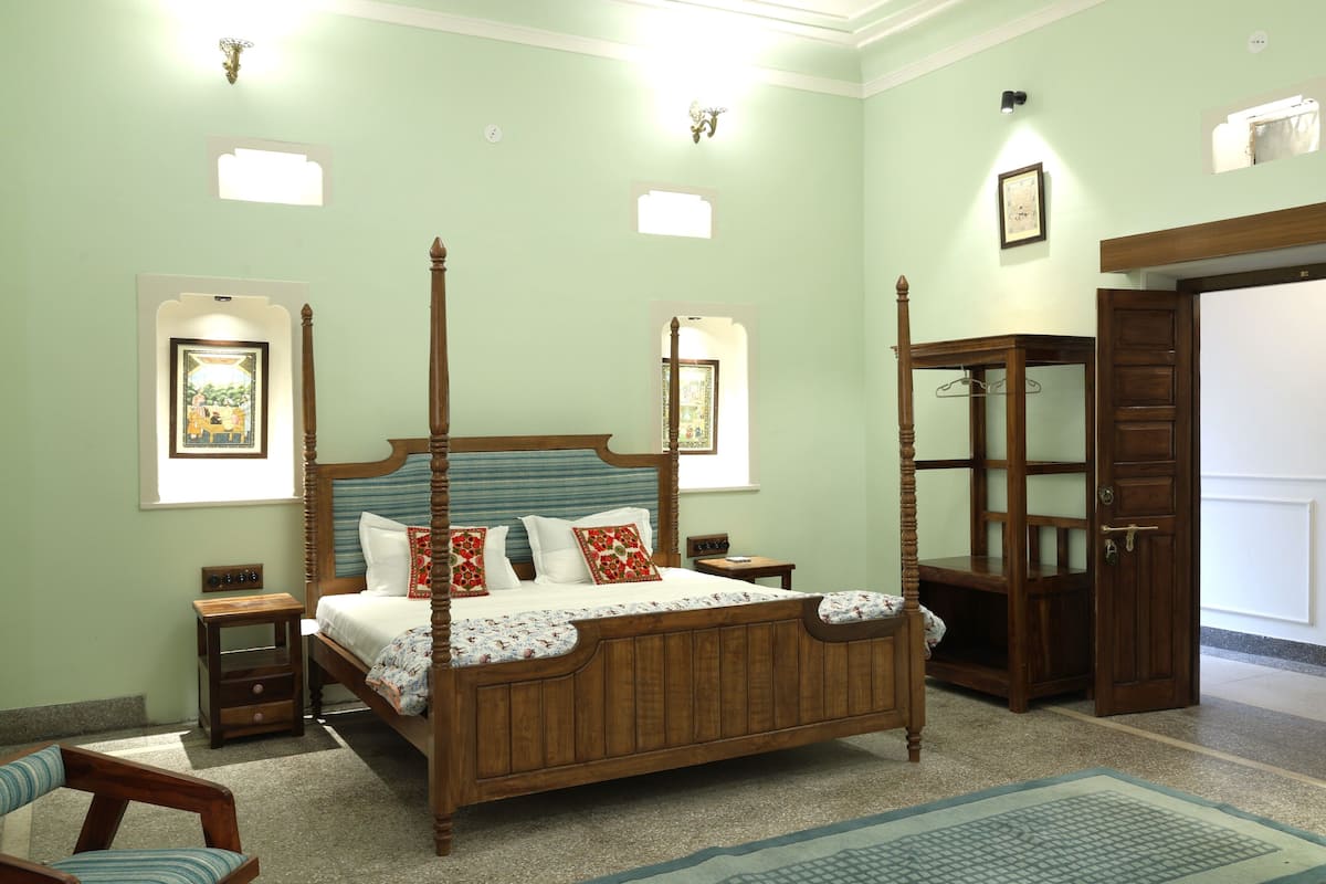 Una cama con dosel de madera con cabecera, una mesita de noche con lámpara, un armario de madera y un cuadro enmarcado en la pared.