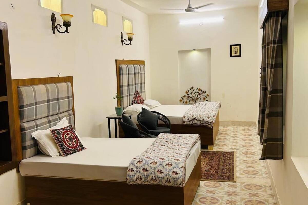 Habitación de hotel con dos camas, ventilador de techo, luces fijadas a la pared y suelo con baldosas estampadas.