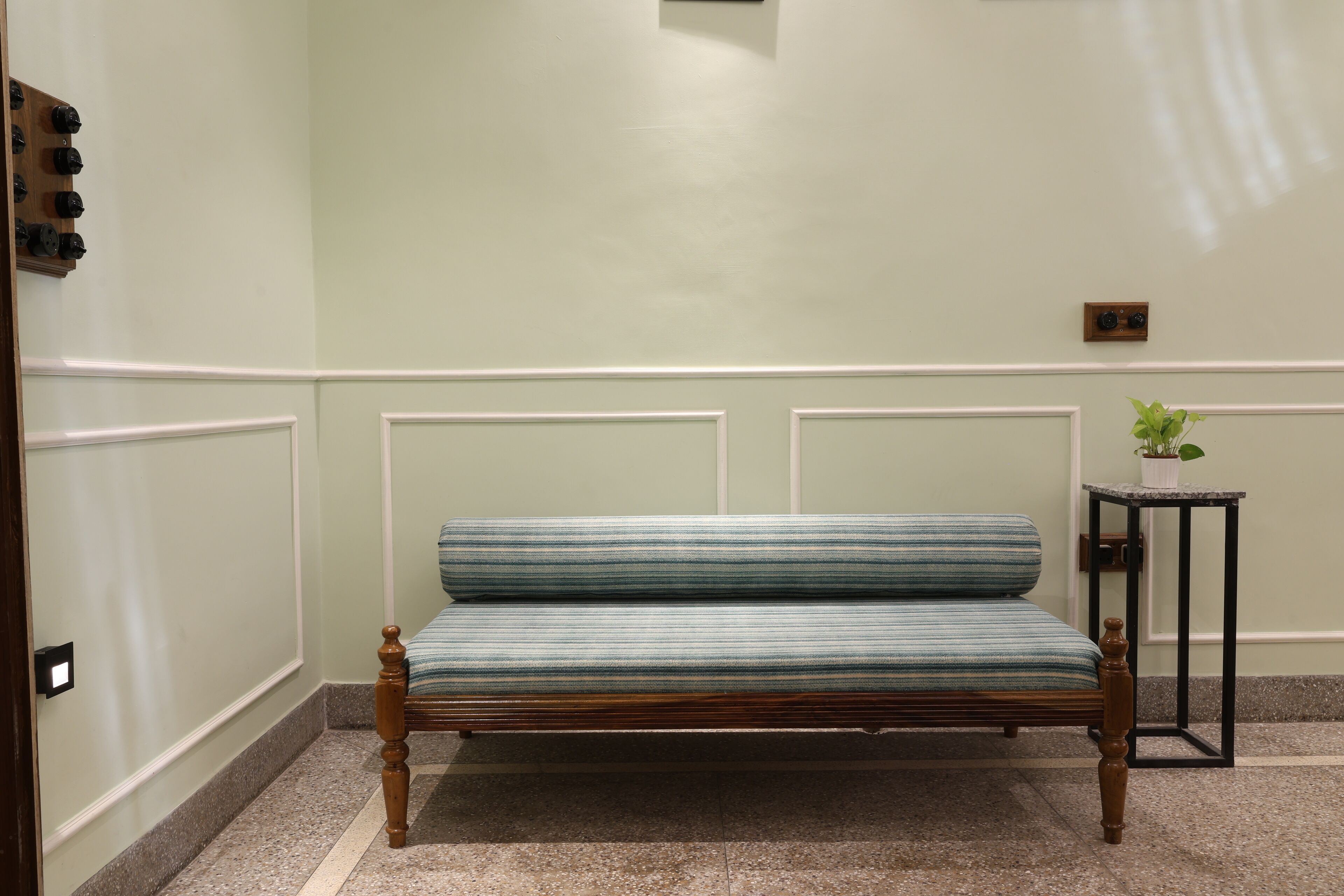 A bench with a striped cushion in a hallway with white wainscoting and a small potted plant on a side table.