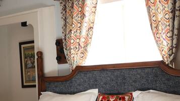 Un lit avec une couvre-lit à motifs, une tête de lit en bois et une fenêtre ornée de rideaux à motifs.