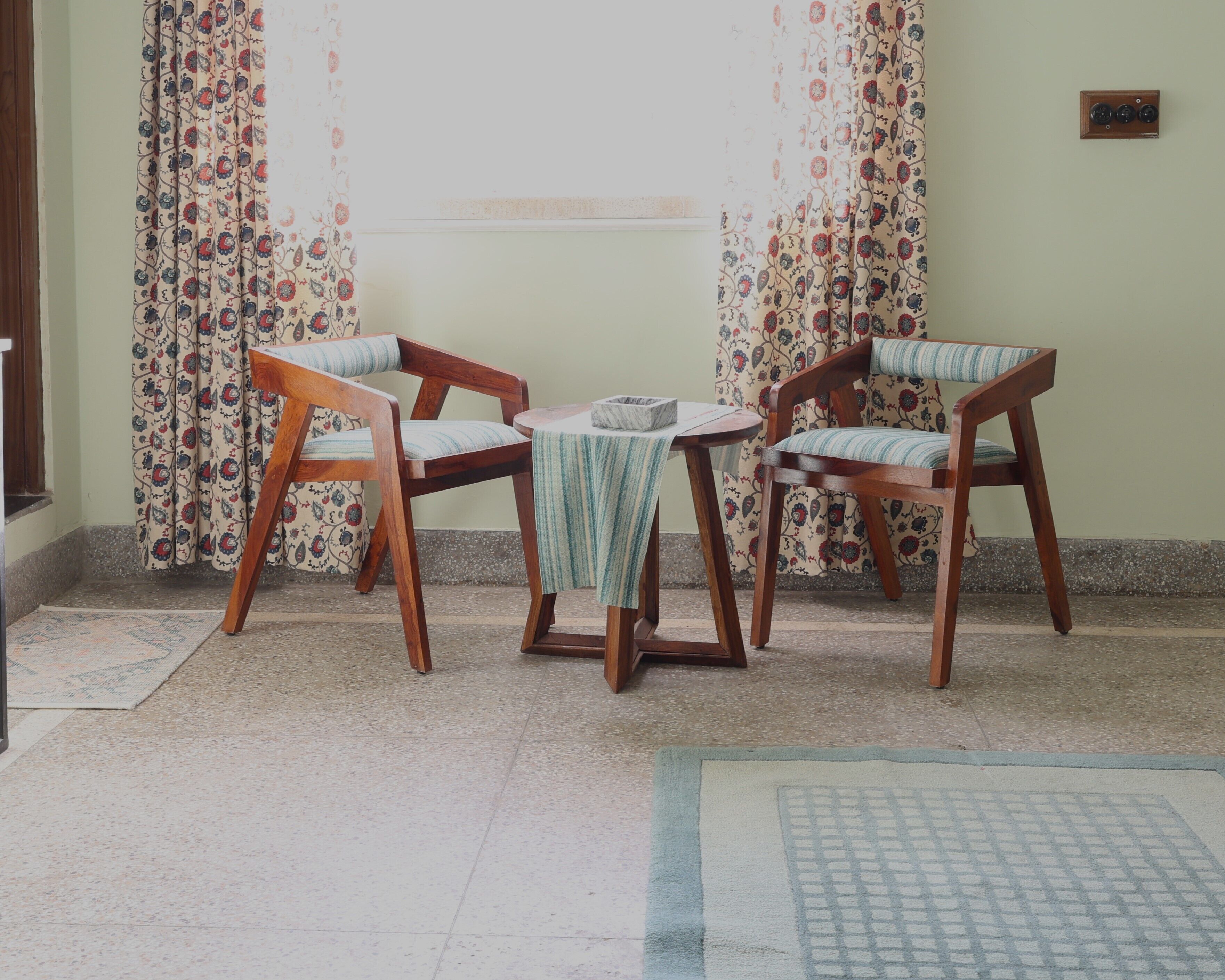 Una habitación con dos sillas de madera, una mesita pequeña y una cortina estampada.