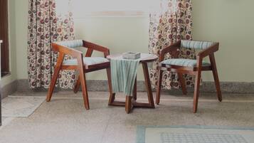 Una habitación con dos sillas de madera, una mesita pequeña y una cortina estampada.