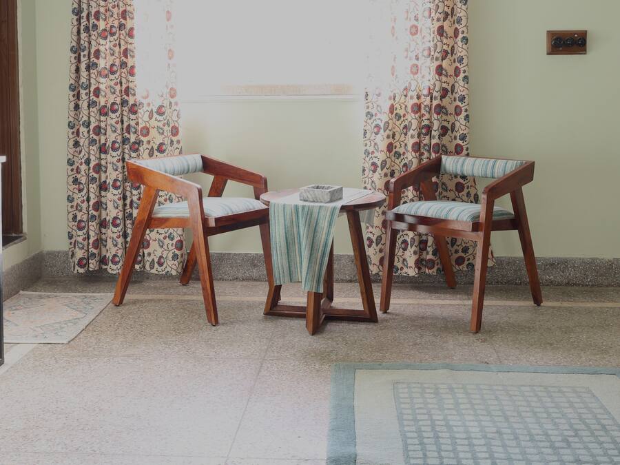 Una habitación con dos sillas de madera, una mesita pequeña y una cortina estampada.