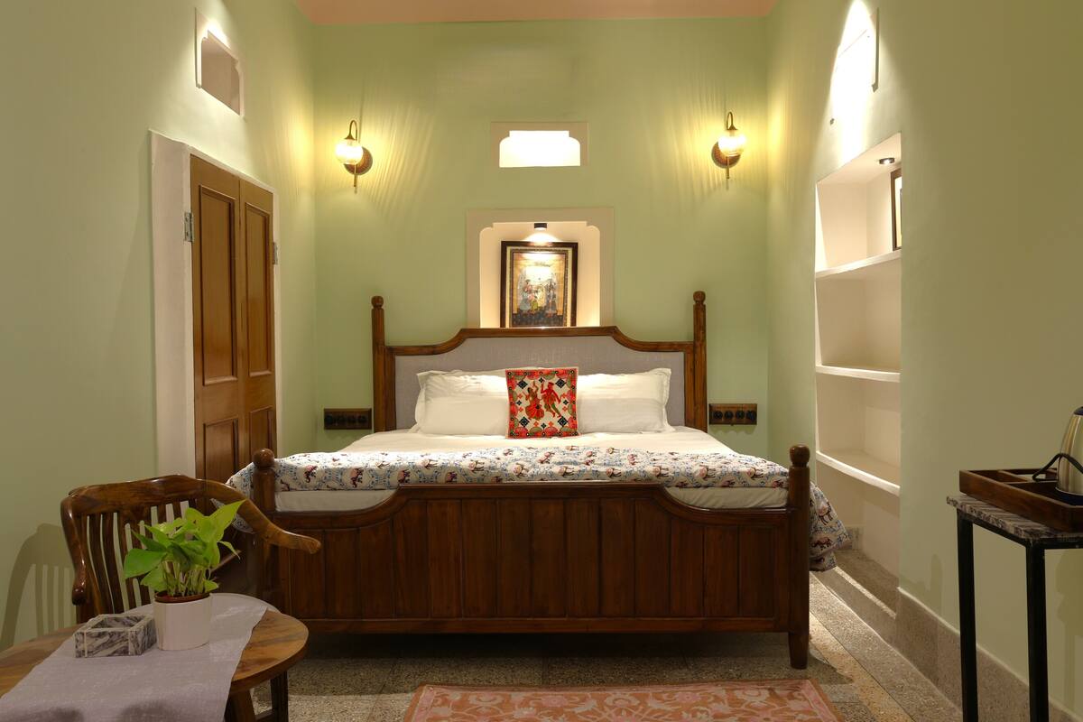 Un dormitorio con cama de madera, mesita de noche, silla, planta en maceta y un cuadro colgado en la pared.