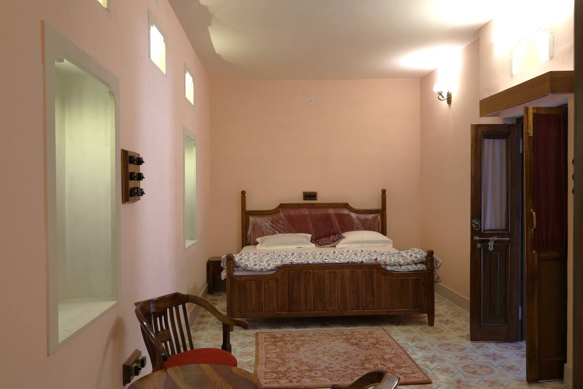 Un dormitorio con una cama de madera, una silla, una mesita y una puerta.