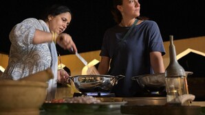 Two people cooking at an outdoor table with various cooking utensils and a gas stove. - House Of Amer (Amer)