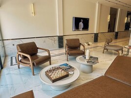 Un vestíbulo con piso de mármol, sillones de cuero, una mesa de ajedrez y una pantalla de televisión.