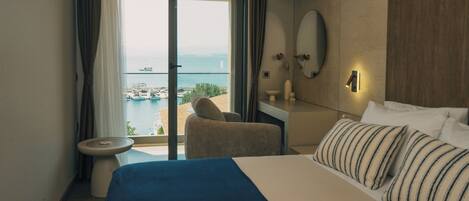 A hotel room with a bed, a desk, a chair, a view of the sea, and a balcony.