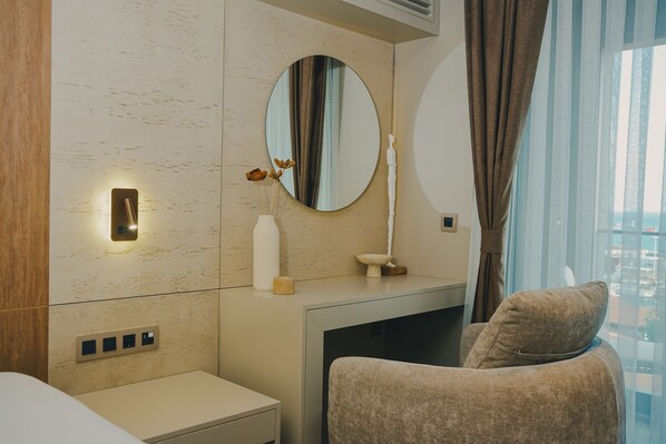 Une chambre d’hôtel moderne au design minimaliste, dotée d’un grand miroir, d’une table de chevet agrémentée d’un vase de fleurs et d’un coin salon confortable avec un coussin.