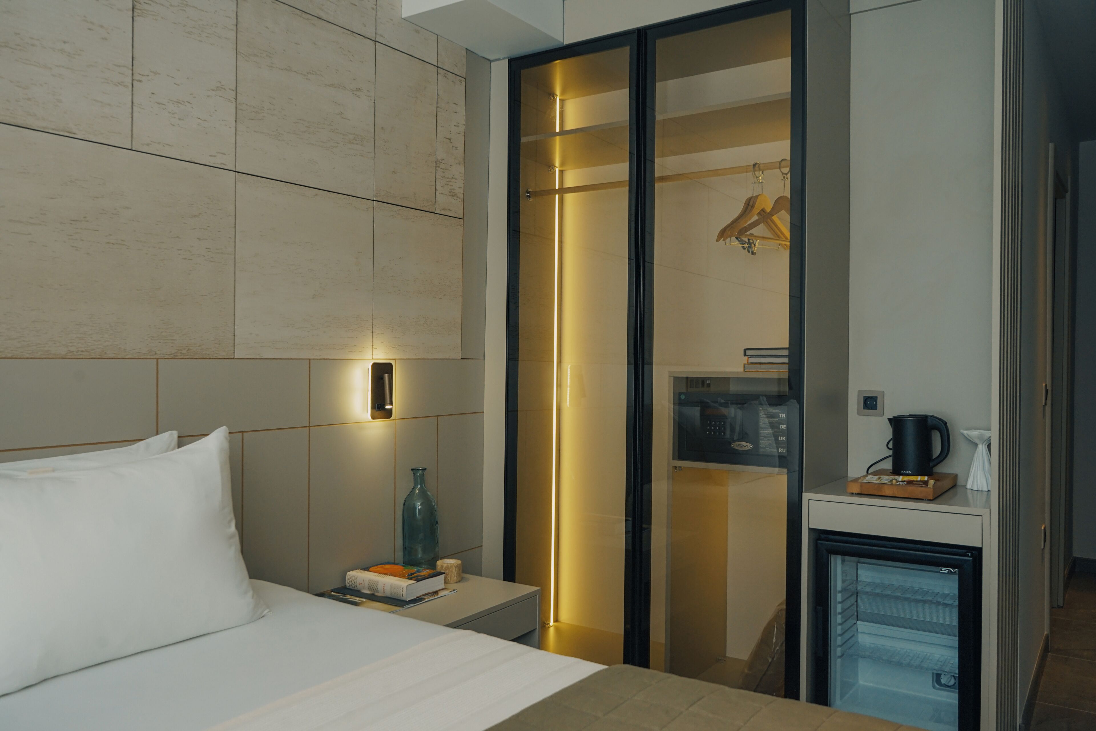 A modern hotel room with a bed, bedside table, and a minibar.