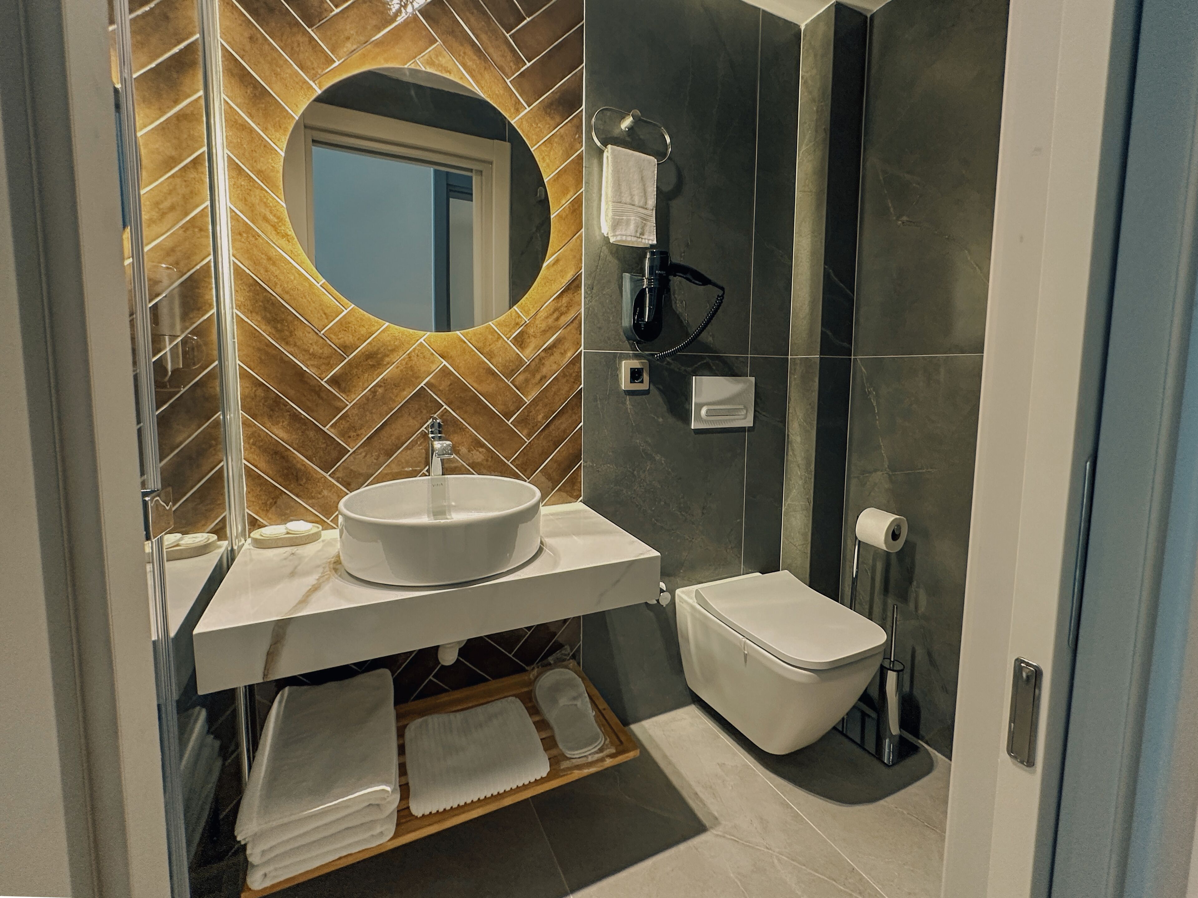 A modern bathroom with a round mirror, white sink, and toilet.
