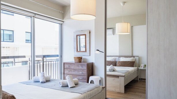 A modern bedroom with a large bed, a dresser, and a mirror. - Berries 1-BR Apt in Larnaca (Larnaca)