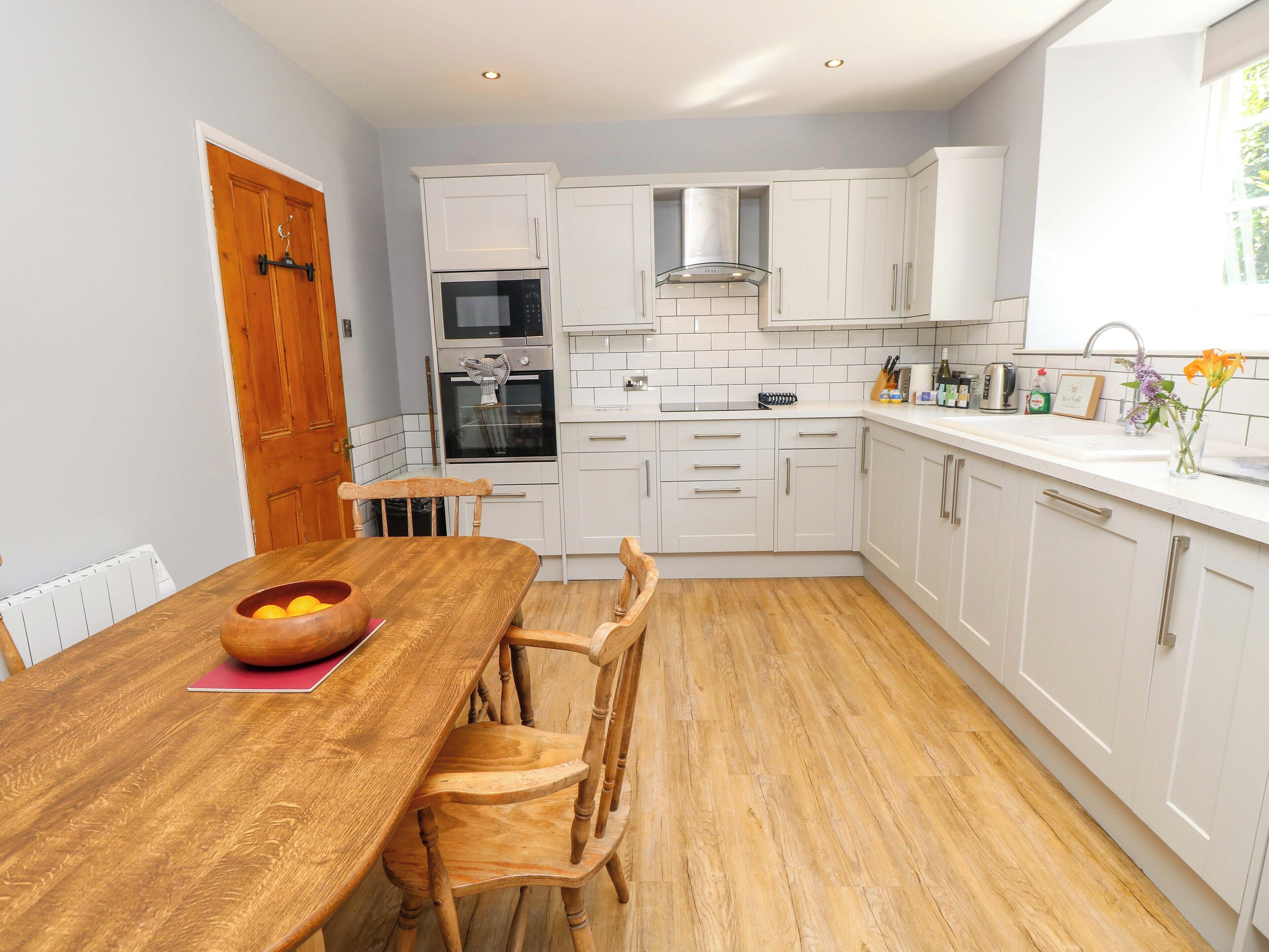 A modern kitchen with white cabinets, a wooden dining table, and a built-in oven.