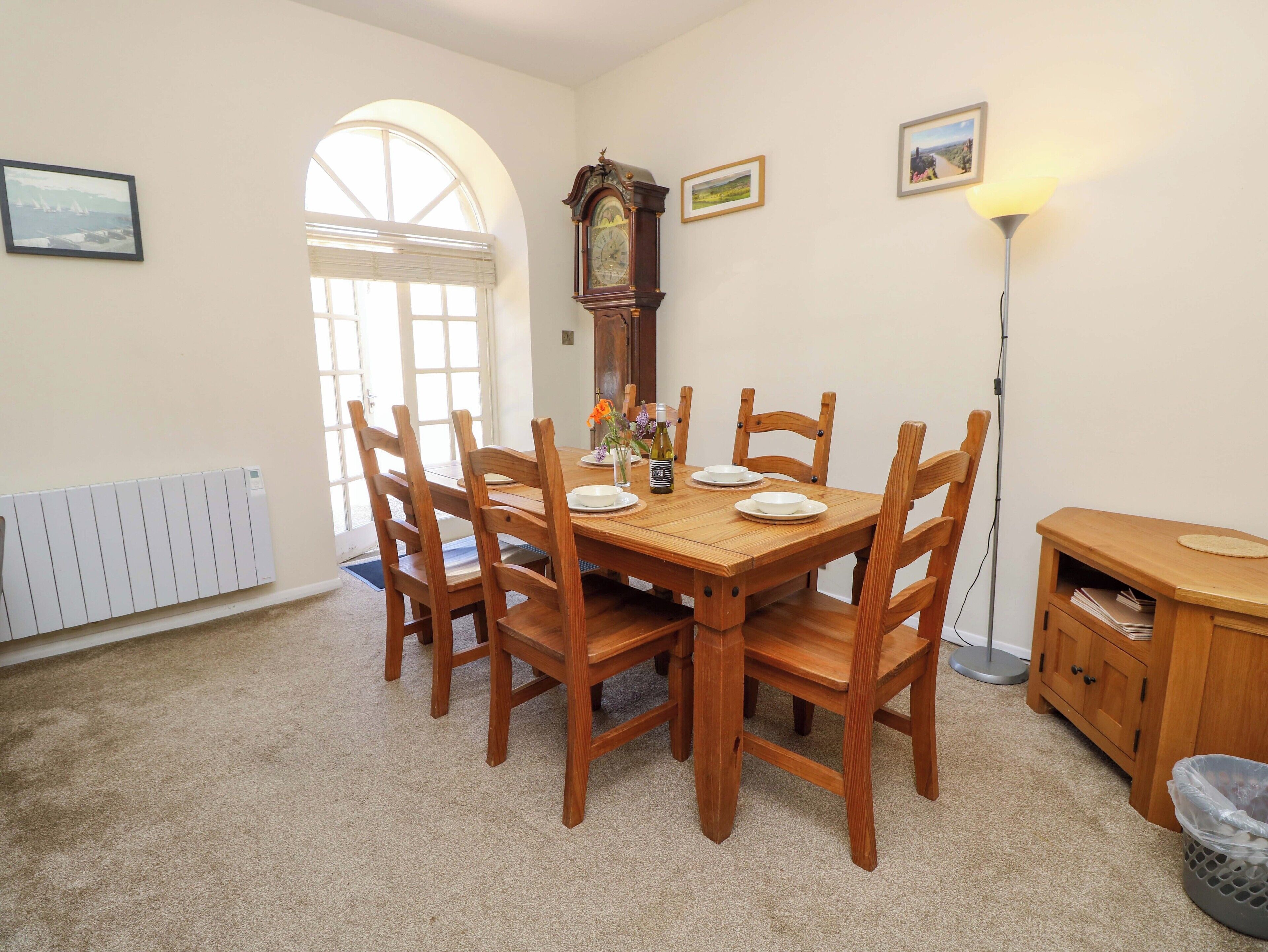 Uma sala de jantar com mesa e cadeiras de madeira, um relógio antigo e um abajur.